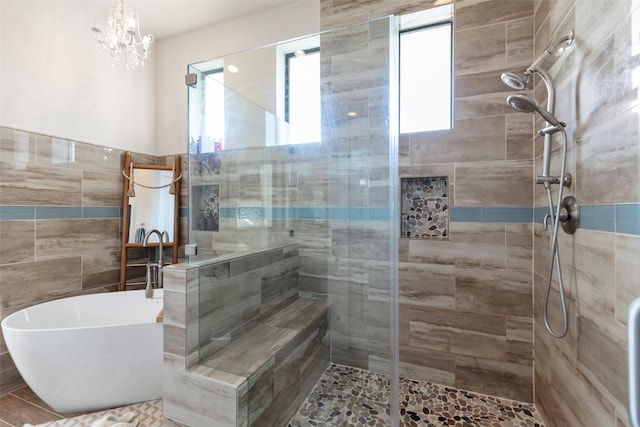 full bathroom with tile walls, a freestanding tub, a notable chandelier, and a shower stall