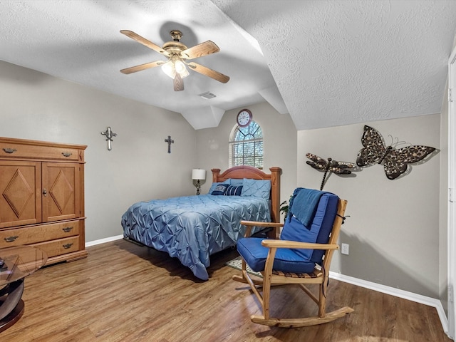 bedroom featuring light wood finished floors, visible vents, vaulted ceiling, a textured ceiling, and baseboards