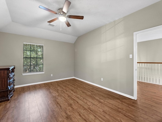 spare room with visible vents, a ceiling fan, vaulted ceiling, wood finished floors, and baseboards