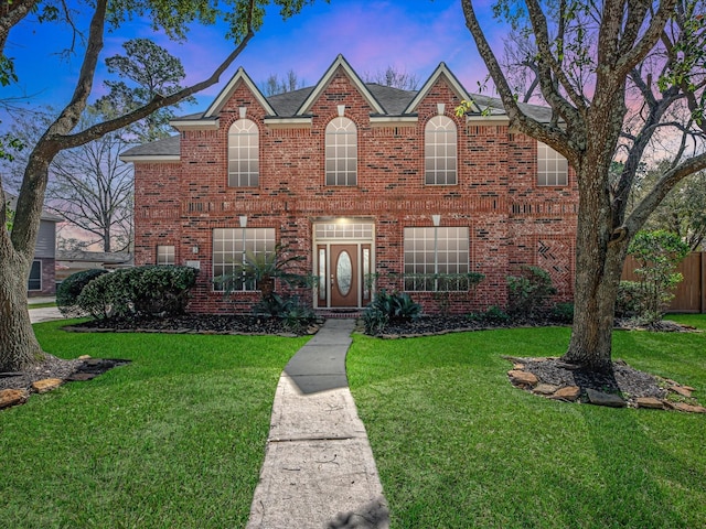 traditional-style house featuring a shingled roof, a front yard, and brick siding