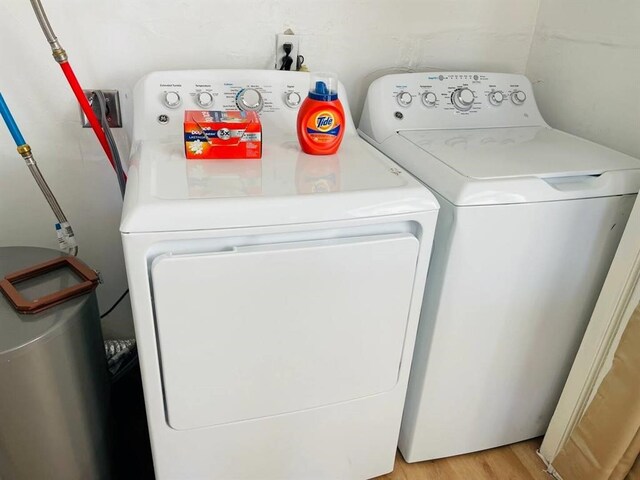 clothes washing area with washing machine and dryer and light wood-style flooring