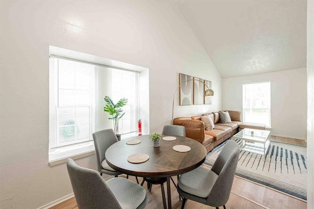 dining room featuring lofted ceiling, light wood finished floors, and baseboards