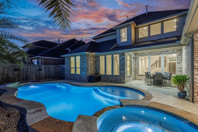 pool at dusk with a pool with connected hot tub, fence, and a patio