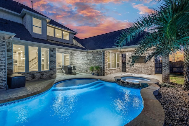 pool at dusk with a patio area, a pool with connected hot tub, and fence