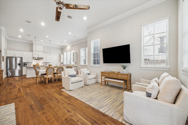 living area featuring dark wood-type flooring, a healthy amount of sunlight, visible vents, and a ceiling fan