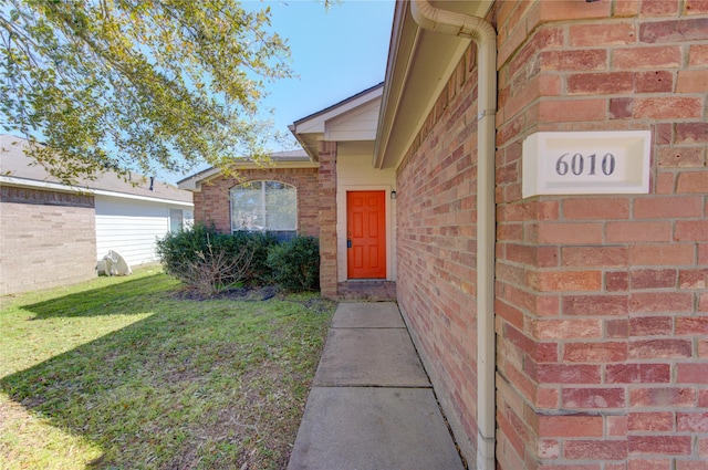 doorway to property with brick siding and a yard