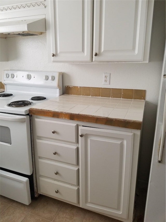 kitchen with white electric range, under cabinet range hood, tile countertops, light tile patterned flooring, and white cabinets