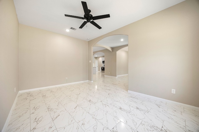 unfurnished room with a ceiling fan, arched walkways, marble finish floor, and baseboards