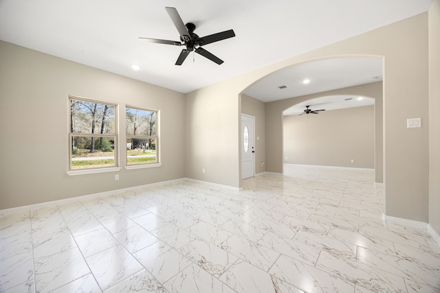 empty room with arched walkways, marble finish floor, recessed lighting, a ceiling fan, and baseboards