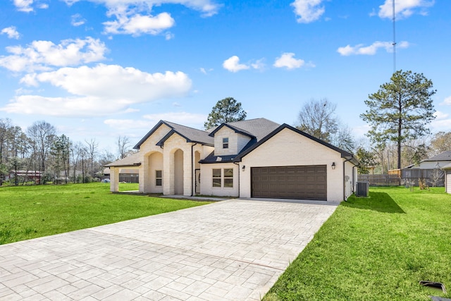 french country home with central AC unit, an attached garage, brick siding, fence, and a front yard