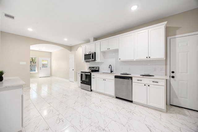 kitchen with arched walkways, marble finish floor, stainless steel appliances, visible vents, and backsplash