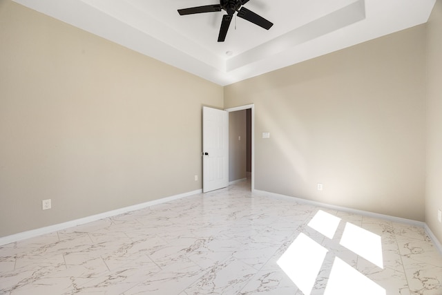 unfurnished room featuring marble finish floor, ceiling fan, baseboards, and a raised ceiling