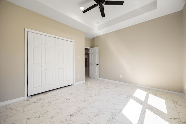 unfurnished bedroom featuring marble finish floor, a tray ceiling, and baseboards