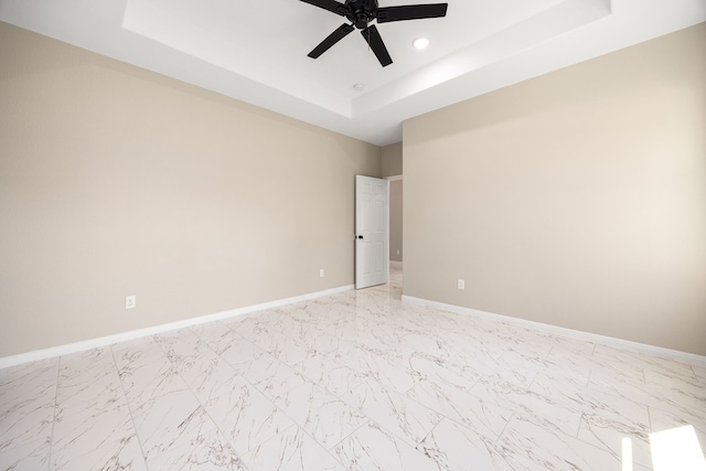 spare room featuring a tray ceiling, marble finish floor, recessed lighting, a ceiling fan, and baseboards