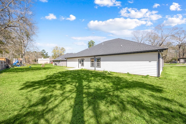 rear view of house featuring a shingled roof, fence, a lawn, and a playground