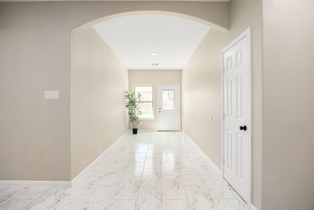 hallway featuring arched walkways, marble finish floor, and baseboards