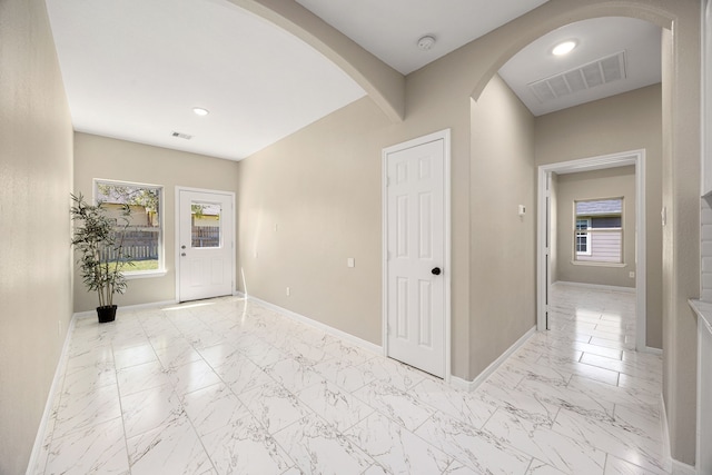 foyer with marble finish floor, baseboards, visible vents, and arched walkways