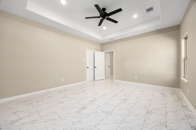 spare room featuring a tray ceiling, visible vents, and baseboards