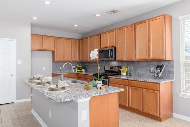 kitchen with a kitchen island with sink, a sink, visible vents, appliances with stainless steel finishes, and decorative backsplash