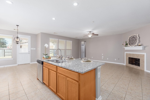 kitchen with light tile patterned floors, a tile fireplace, an island with sink, a sink, and stainless steel dishwasher