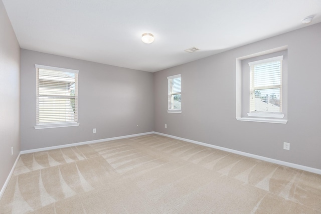 empty room featuring baseboards, visible vents, and light colored carpet