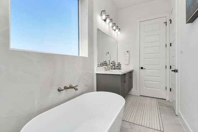 bathroom with marble finish floor, a freestanding bath, and vanity