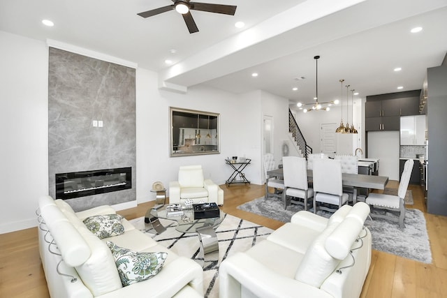 living room with ceiling fan with notable chandelier, recessed lighting, a tiled fireplace, light wood-type flooring, and stairs