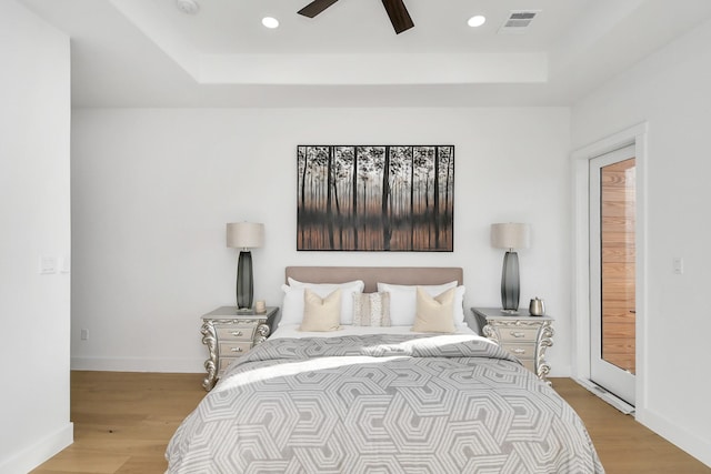 bedroom with light wood finished floors, a raised ceiling, and visible vents