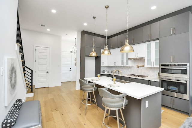 kitchen featuring light wood finished floors, stainless steel appliances, visible vents, decorative backsplash, and a sink