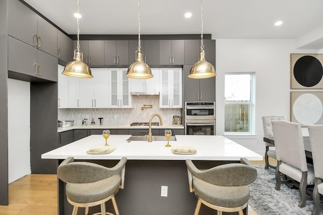 kitchen featuring double oven, a sink, a kitchen breakfast bar, light countertops, and backsplash