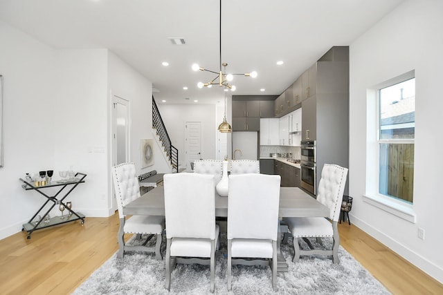 dining room featuring visible vents, a notable chandelier, stairway, and light wood finished floors