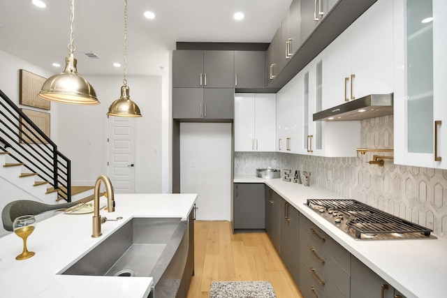 kitchen featuring stainless steel appliances, a sink, under cabinet range hood, and gray cabinetry