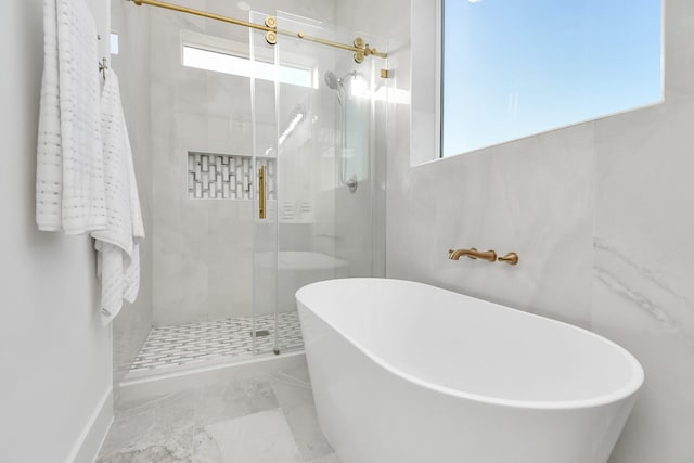 bathroom with marble finish floor, a soaking tub, and a shower stall