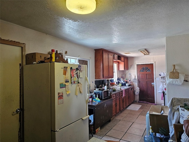 kitchen featuring light tile patterned floors, a textured wall, a textured ceiling, a sink, and freestanding refrigerator