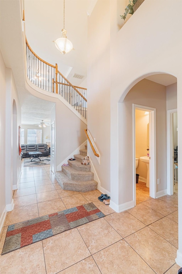 staircase with tile patterned flooring, visible vents, arched walkways, and baseboards