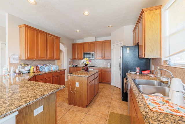 kitchen featuring arched walkways, light tile patterned floors, a sink, appliances with stainless steel finishes, and light stone countertops