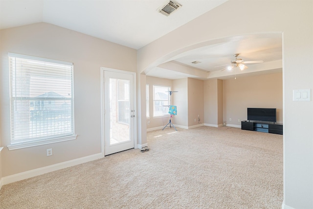 unfurnished living room featuring baseboards, visible vents, arched walkways, a raised ceiling, and carpet flooring