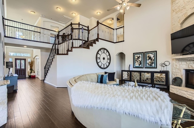 bedroom featuring baseboards, arched walkways, a towering ceiling, dark wood-style floors, and a fireplace