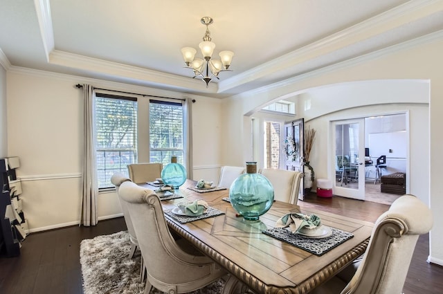 dining area featuring arched walkways, a tray ceiling, dark wood-type flooring, and a chandelier