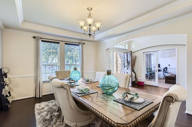 dining area with arched walkways, dark wood-style flooring, a tray ceiling, and a notable chandelier