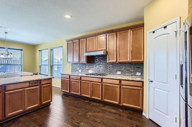 kitchen with dark wood-style flooring, visible vents, brown cabinets, tasteful backsplash, and under cabinet range hood