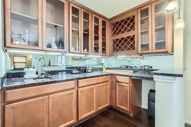 kitchen with a sink, dark wood-style floors, dark stone countertops, and glass insert cabinets