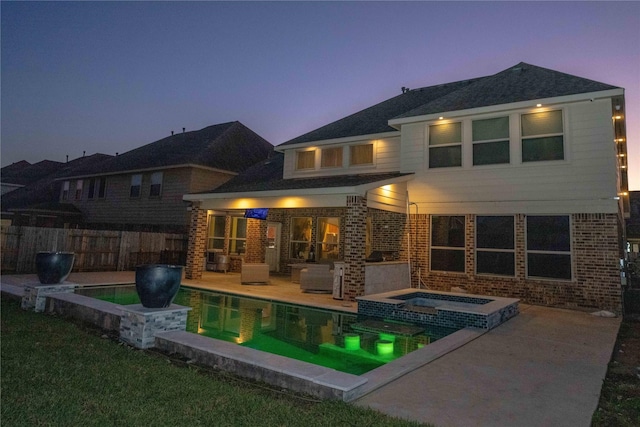 back of property at dusk with a pool with connected hot tub, a patio area, brick siding, and fence