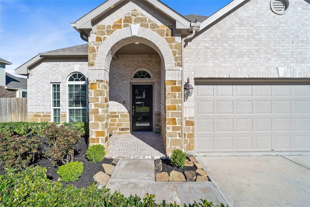 entrance to property featuring a garage, stone siding, brick siding, and fence