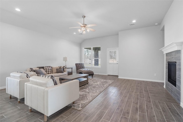 living room with ceiling fan, wood finish floors, a tiled fireplace, and visible vents