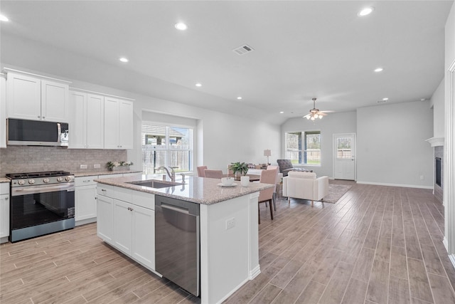 kitchen featuring visible vents, appliances with stainless steel finishes, a glass covered fireplace, light wood-style floors, and a sink