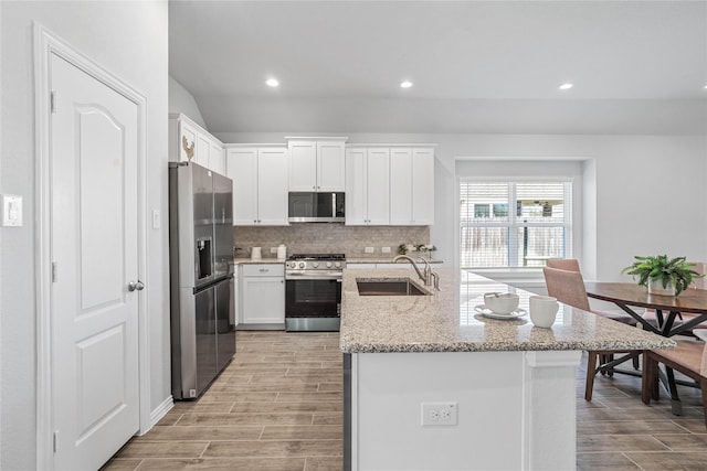 kitchen with wood finish floors, stainless steel appliances, backsplash, white cabinets, and a sink