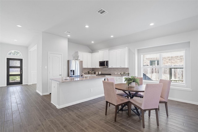 kitchen with an island with sink, visible vents, stainless steel appliances, and dark wood-type flooring