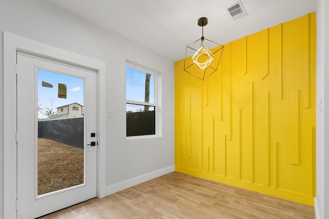 doorway to outside with an inviting chandelier, light wood-style flooring, visible vents, and baseboards