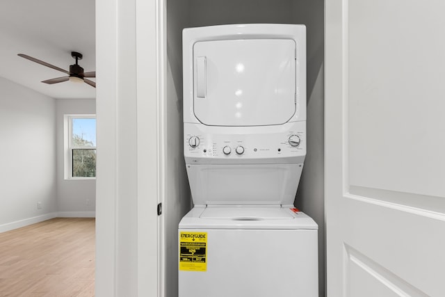 clothes washing area featuring stacked washer / drying machine, a ceiling fan, light wood-type flooring, laundry area, and baseboards